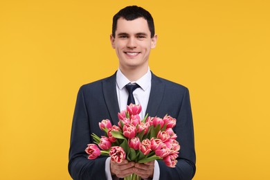 Happy young man with beautiful bouquet on orange background