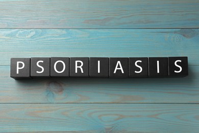 Photo of Word Psoriasis made of black cubes with letters on blue light wooden table, top view