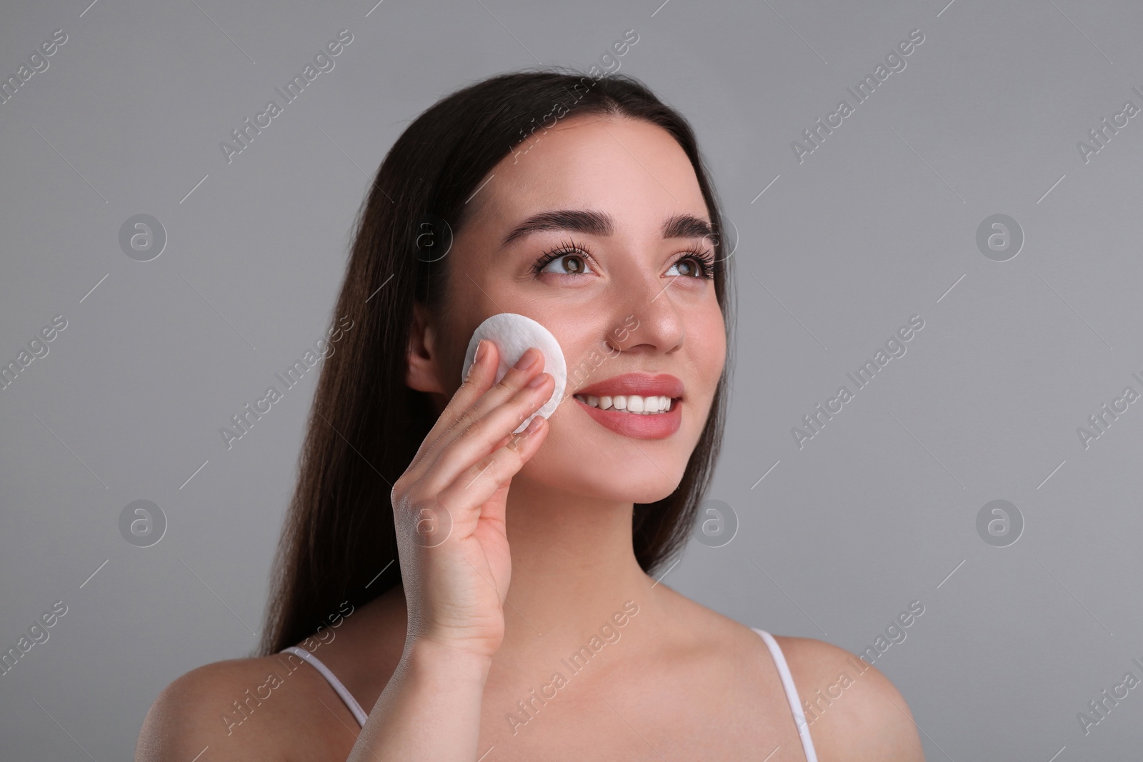 Photo of Beautiful woman removing makeup with cotton pad on gray background