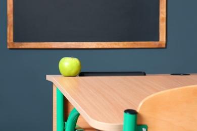 Wooden school desk and apple near blackboard on grey wall