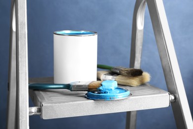 Photo of Can of light blue paint and brushes on metal ladder