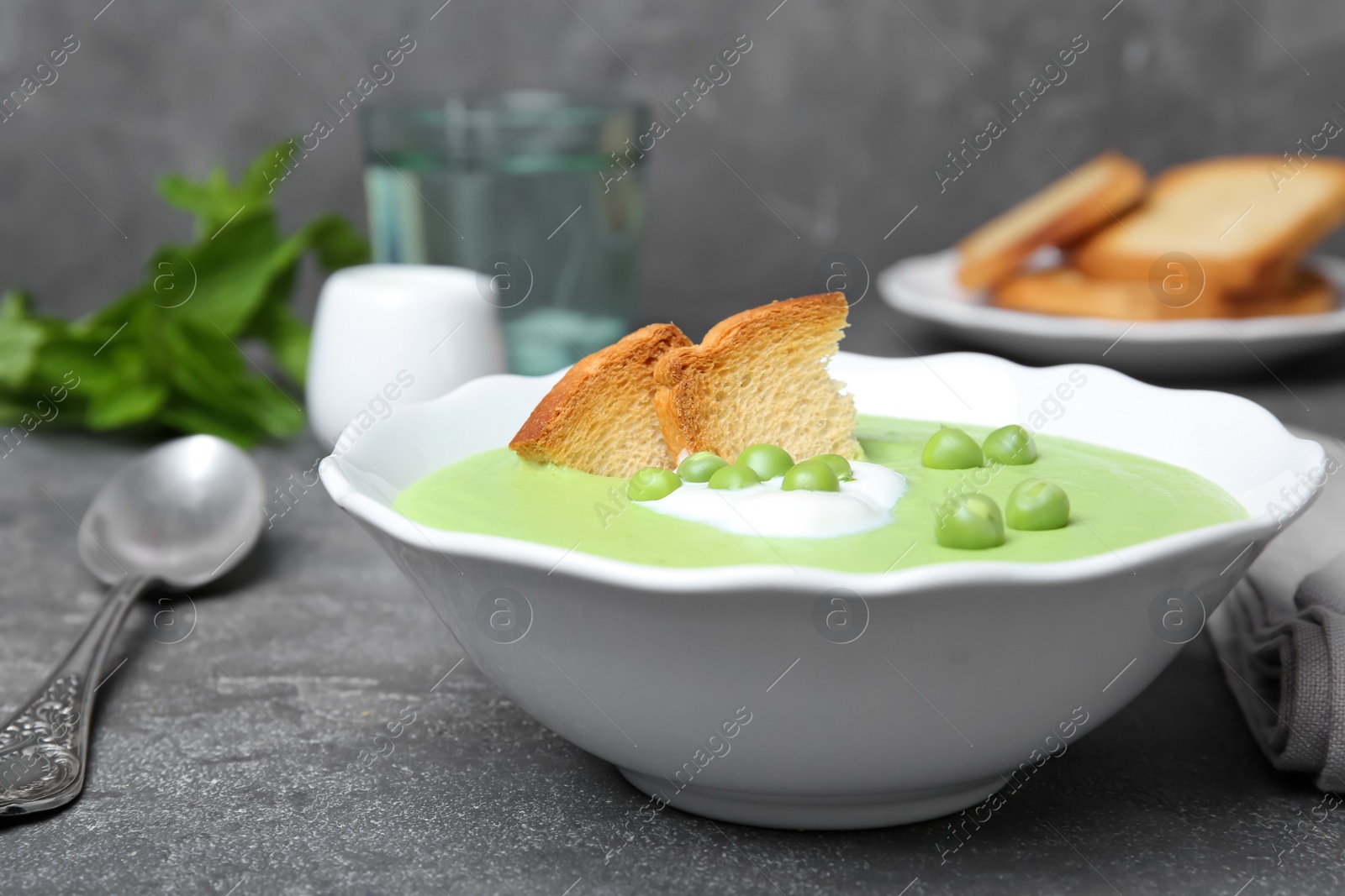 Photo of Green pea soup with croutons in bowl on table