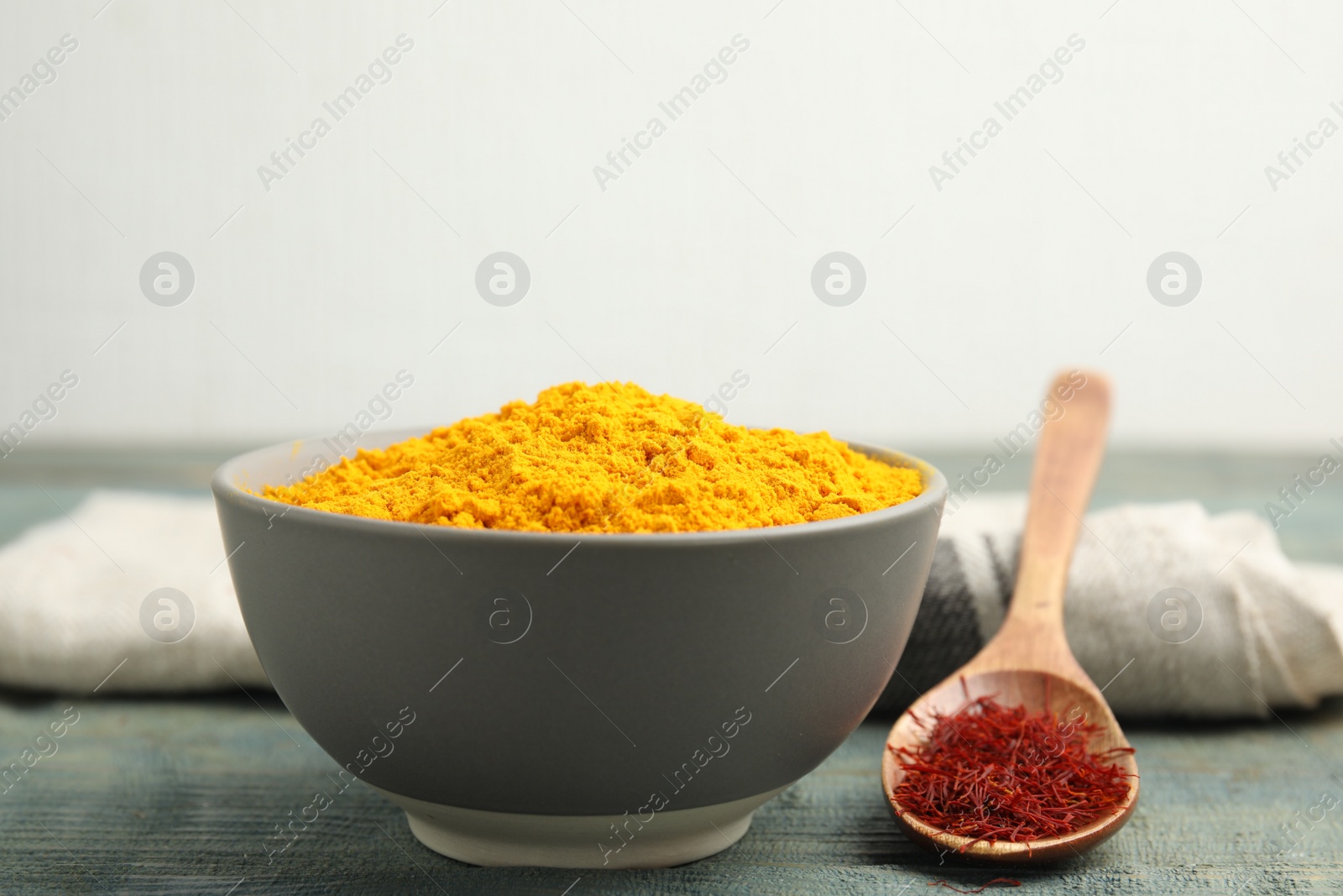 Photo of Bowl of saffron powder and spoon with dried flower stigmas on light blue wooden table