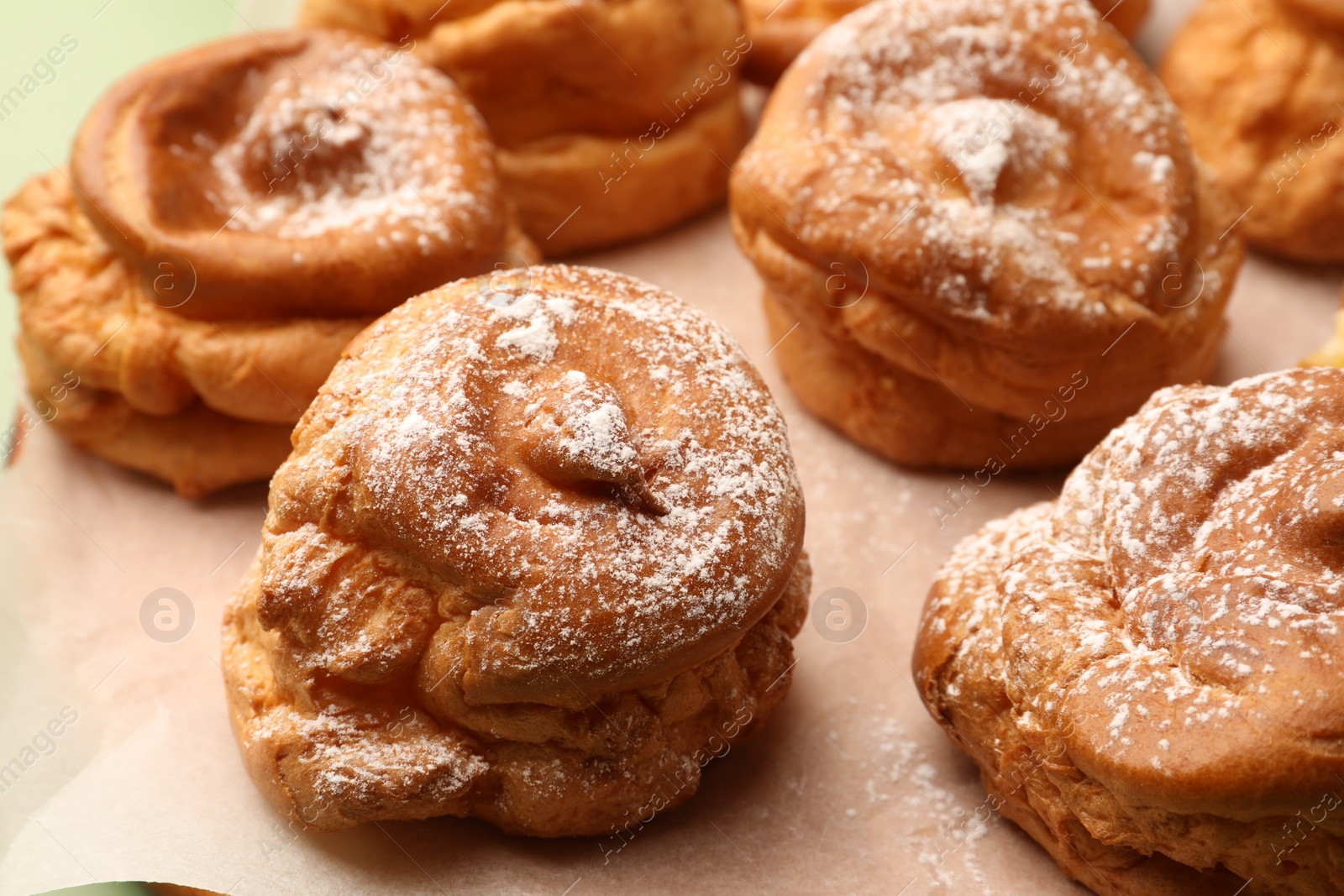 Photo of Delicious profiteroles with powdered sugar on parchment paper, closeup