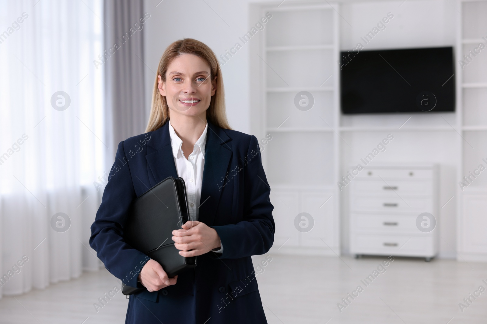 Photo of Happy real estate agent with leather portfolio indoors. Space for text