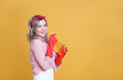 Photo of Beautiful young woman with bottle of detergent singing on orange background. Space for text