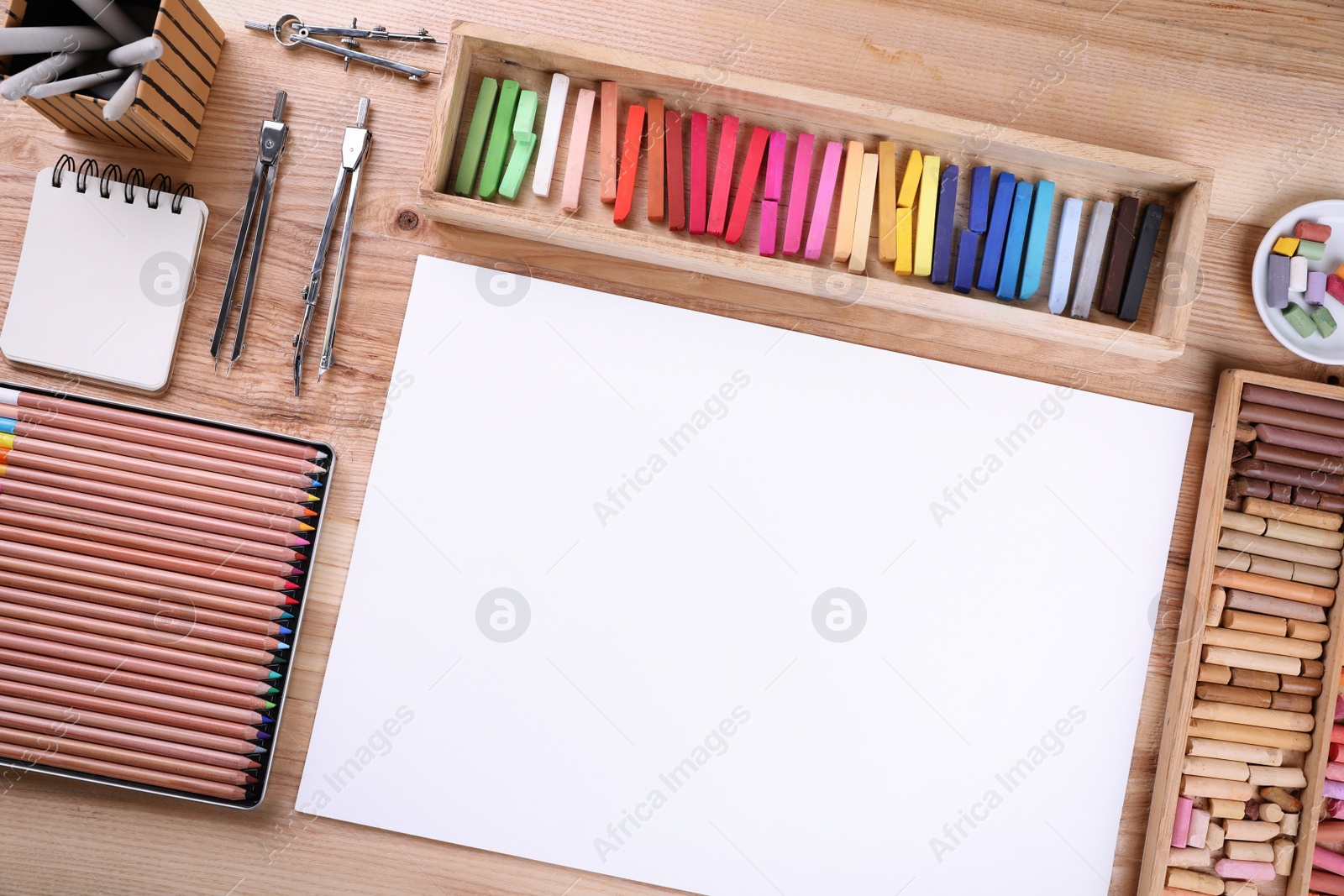 Photo of Layout with blank paper, soft pastels and other drawing supplies on wooden table at artist's workplace, top view. Space for design