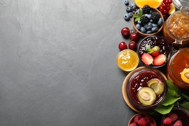 Photo of Jars with different jams and fresh fruits on black table, flat lay. Space for text