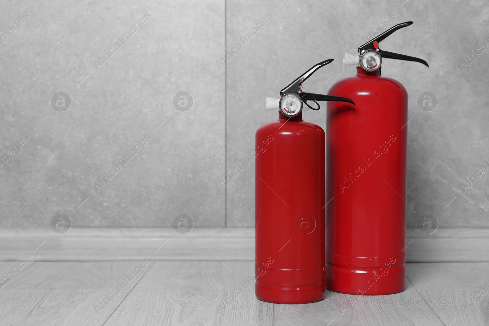 Photo of Fire extinguishers on floor near grey wall, space for text