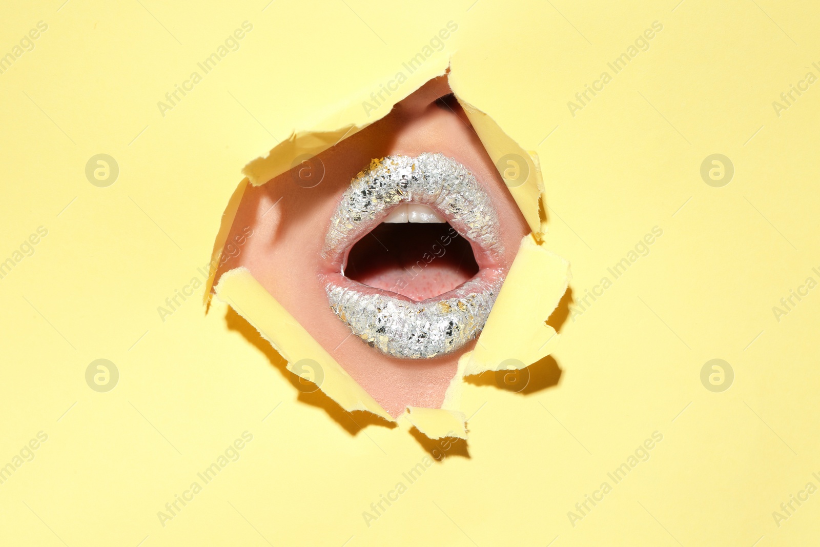 Photo of View of beautiful young woman with creative lips makeup through hole in color paper