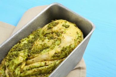 Uncooked pesto bread in baking dish on light blue wooden table, closeup