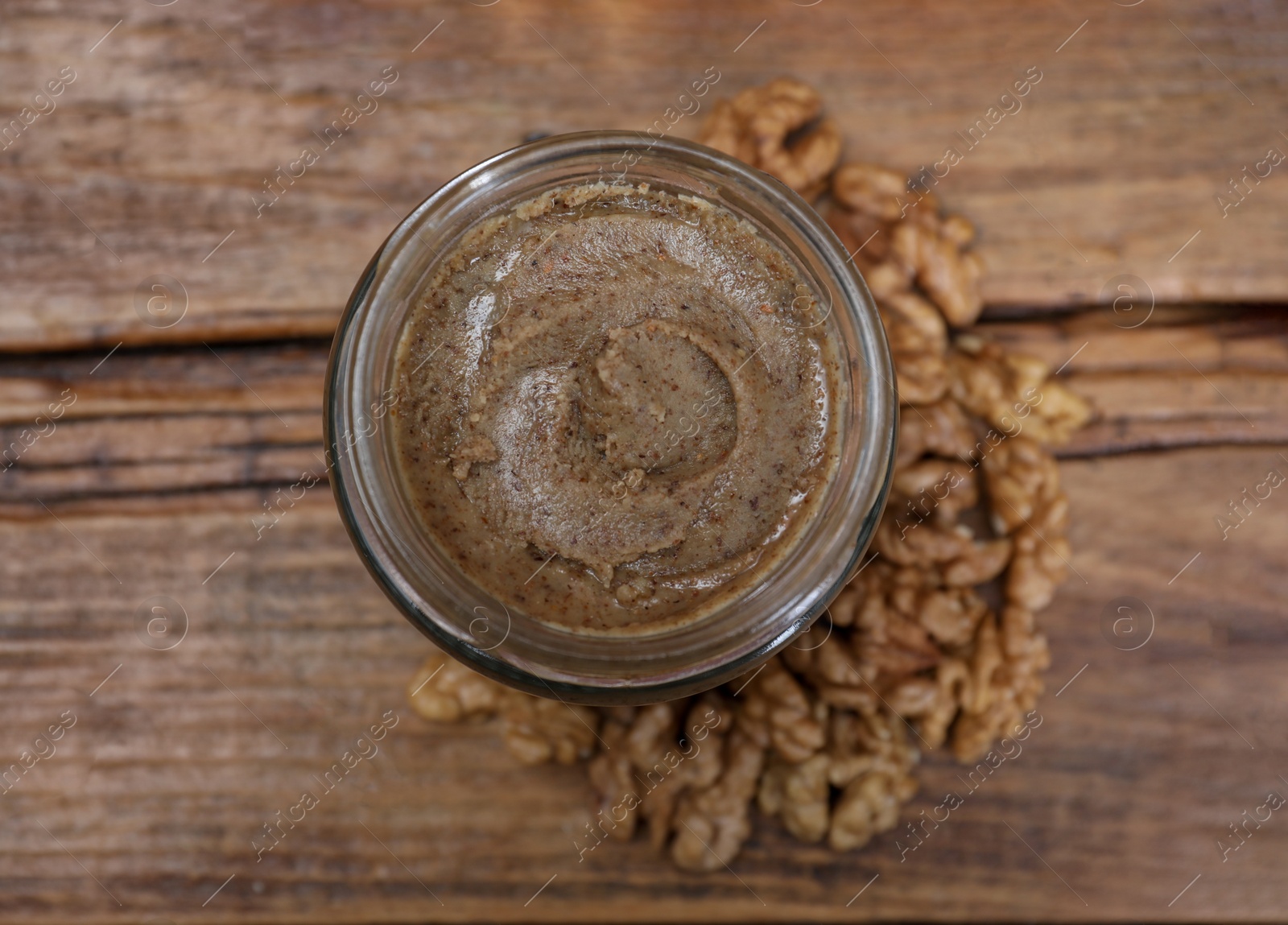 Photo of Tasty walnut nut paste in jar on wooden table, top view