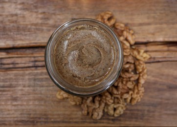 Photo of Tasty walnut nut paste in jar on wooden table, top view