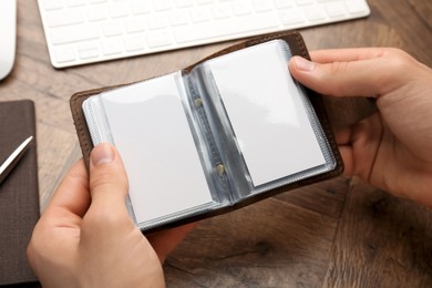 Photo of Man holding leather business card holder with blank cards at wooden table, closeup