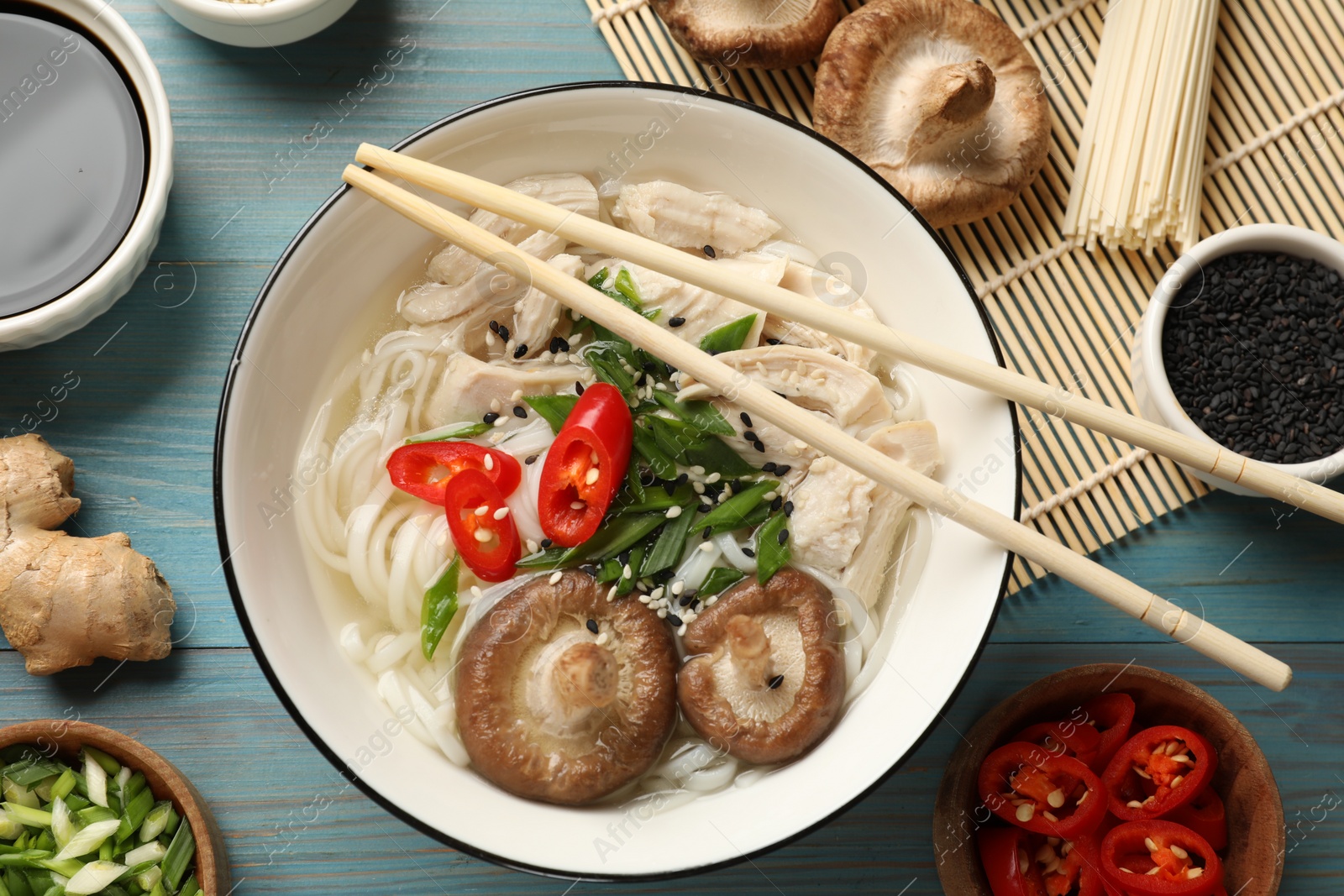 Photo of Delicious ramen with meat and ingredients on light blue wooden table, flat lay. Noodle soup