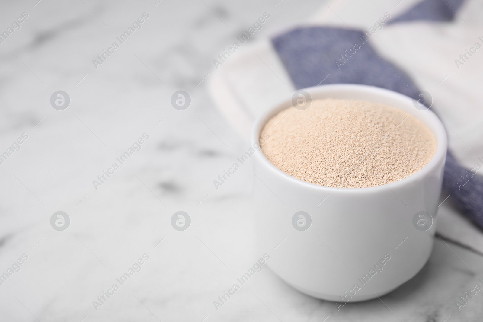 Photo of Granulated yeast in bowl on white marble table, closeup. Space for text