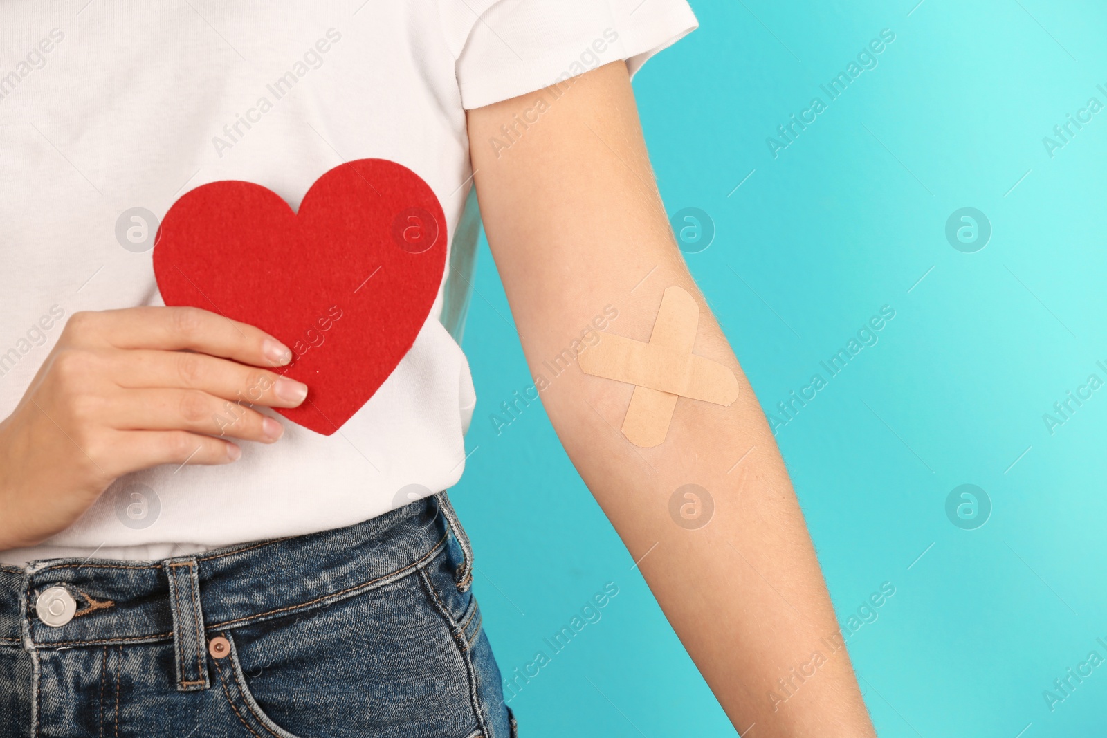 Photo of Woman holding heart near hand with adhesive plasters against color background, closeup. Blood donation