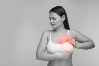 Young woman suffering from breast pain on light grey background. Black and white with color accent effect