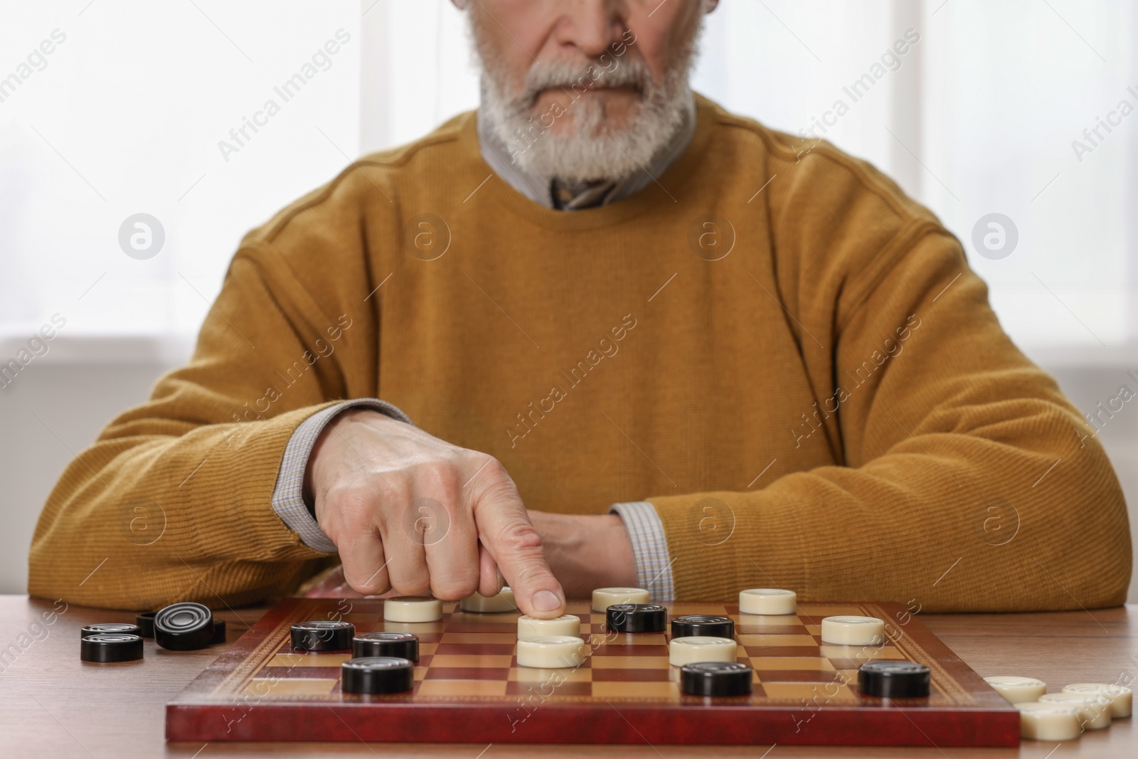 Photo of Playing checkers. Senior man thinking about next move at table in room, closeup