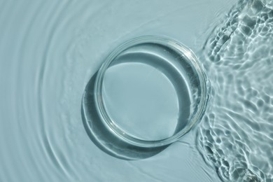 Photo of Stylish presentation for product. Glass podium in water on light blue background, top view