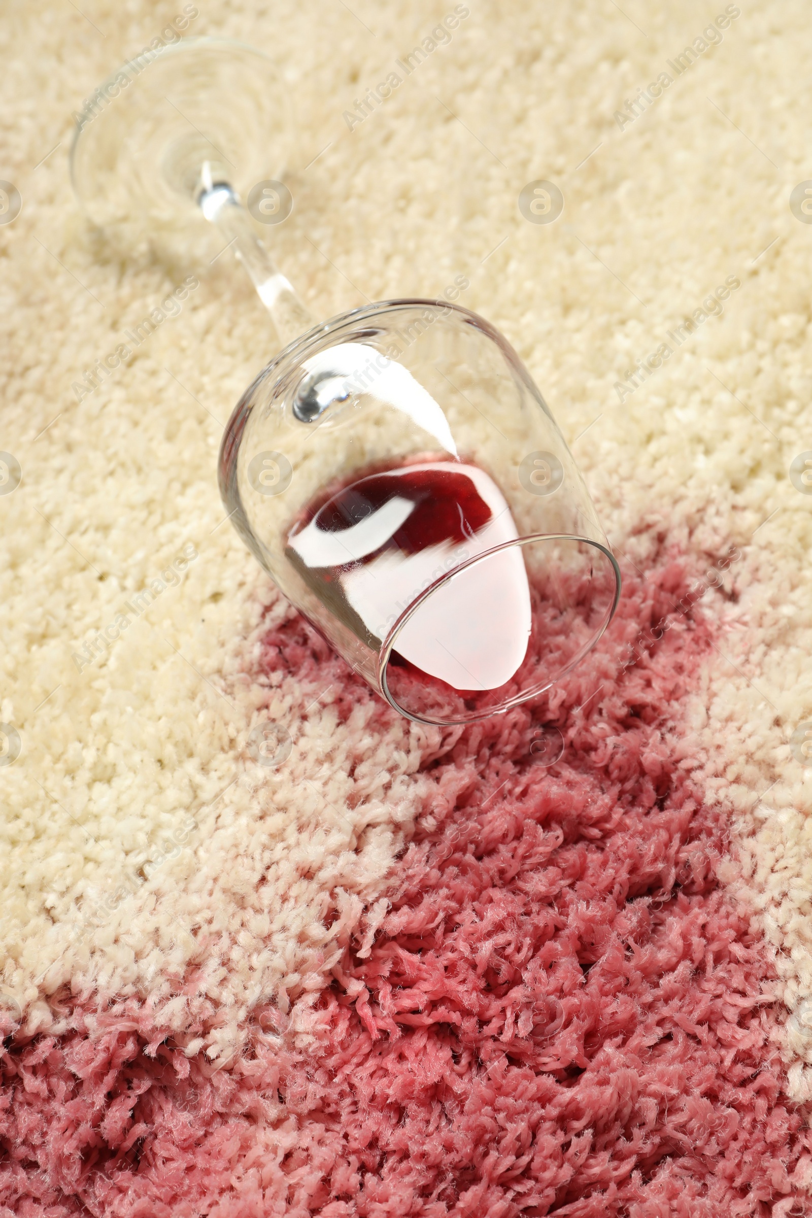 Photo of Overturned glass and spilled red wine on beige carpet, closeup