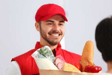 Photo of Male courier delivering food to client on light background
