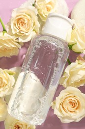Photo of Wet bottle of micellar water and beautiful white roses on pink background, top view