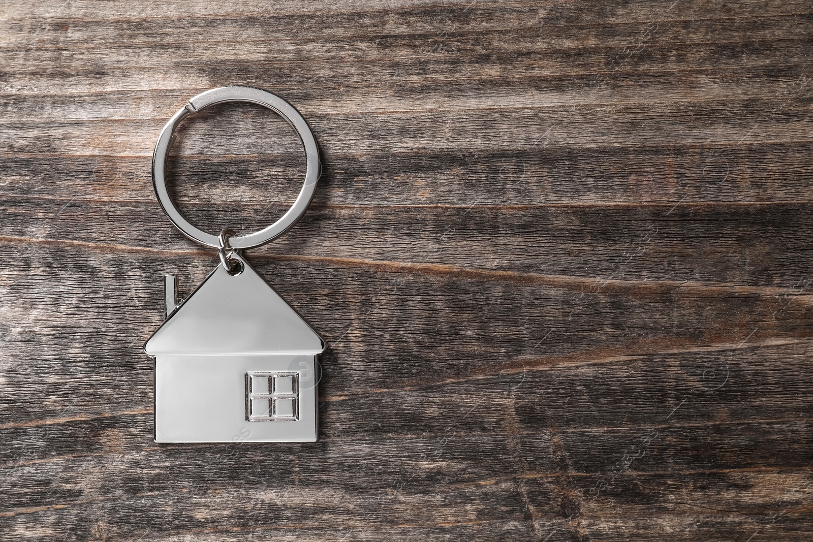 Photo of Metal keychain in shape of house on rustic wooden table, top view. Space for text