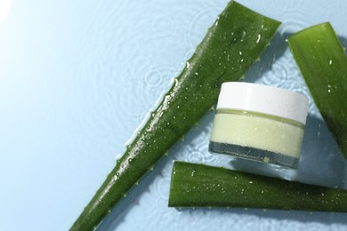 Photo of Jar of cosmetic product and aloe leaves in water on light blue background, flat lay