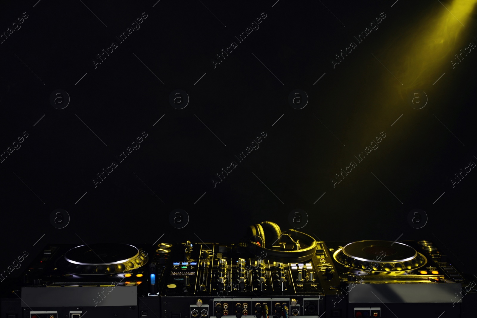 Photo of Modern DJ controller and headphones under beam of light on black background