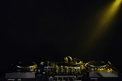 Photo of Modern DJ controller and headphones under beam of light on black background