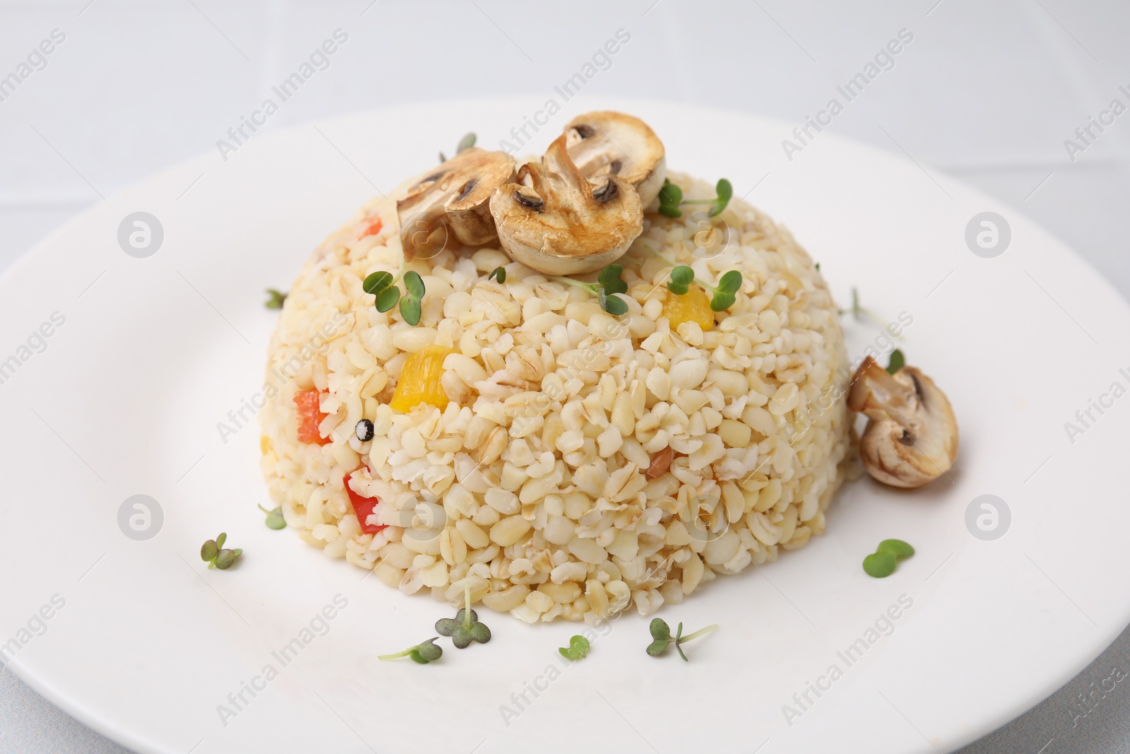 Photo of Delicious bulgur with vegetables, mushrooms and microgreens on table, closeup