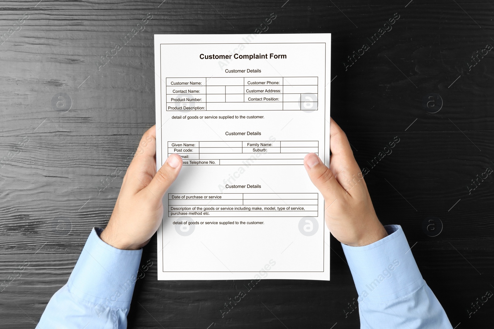 Image of Man holding complaint form at black wooden table, top view
