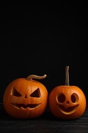Photo of Scary jack o'lanterns made of pumpkins on wooden table against black background, space for text. Halloween traditional decor