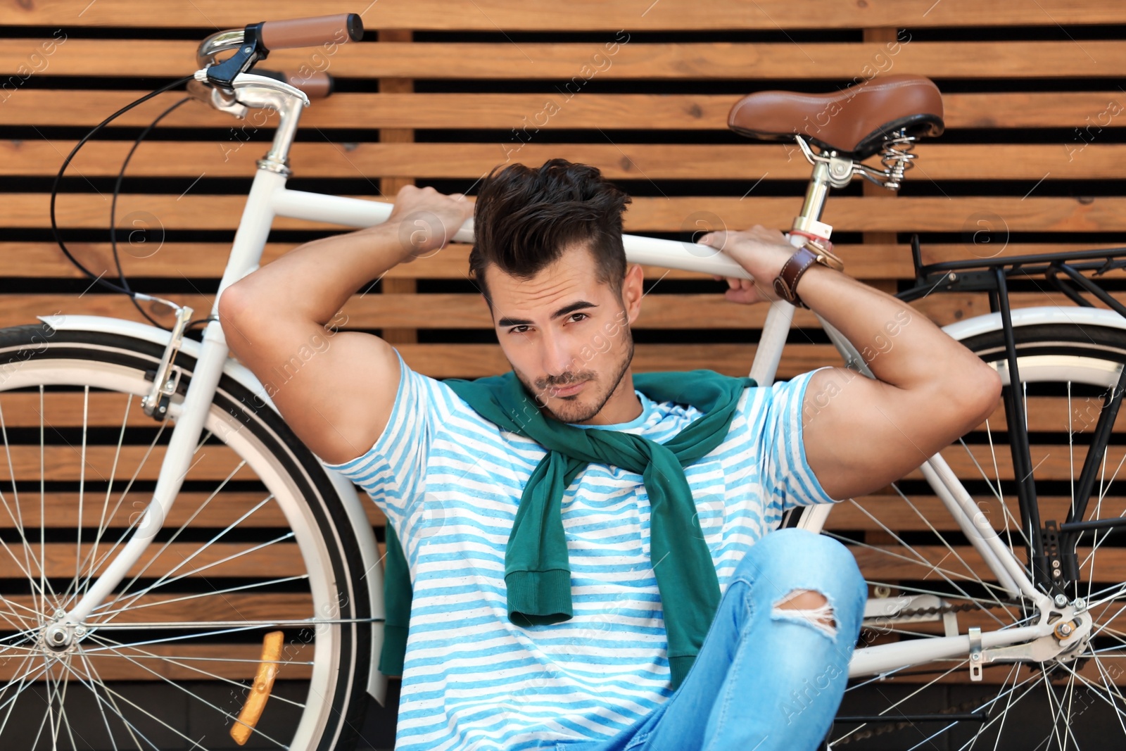 Photo of Handsome young hipster man with bicycle near wooden wall outdoors