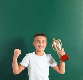 Happy boy with golden winning cup on near chalkboard