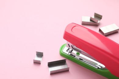 Photo of Bright stapler with staples on pink background, space for text