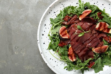 Plate of tasty bresaola salad with figs, sun-dried tomatoes and balsamic vinegar on grey table, top view. Space for text