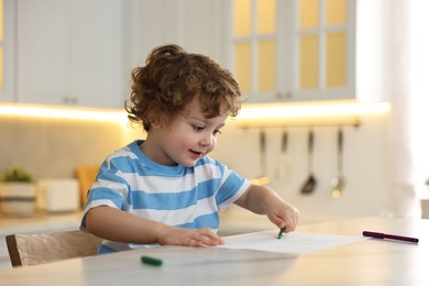 Cute little boy drawing with marker at table in kitchen