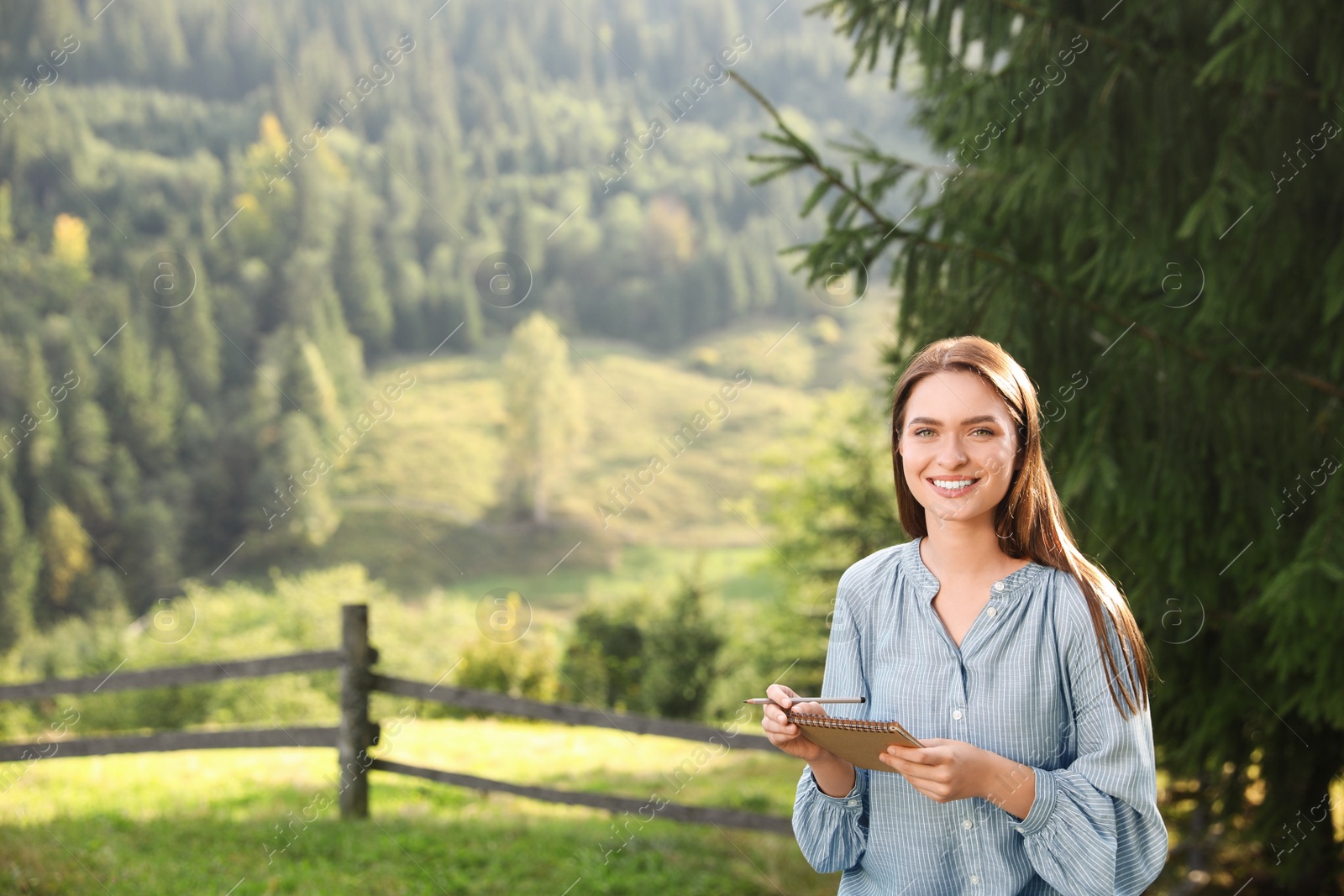 Photo of Beautiful young woman drawing with pencil in notepad outdoors on sunny day