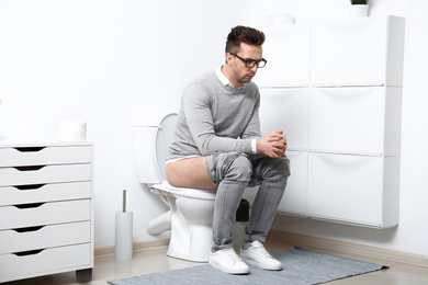 Photo of Upset man sitting on toilet bowl in bathroom