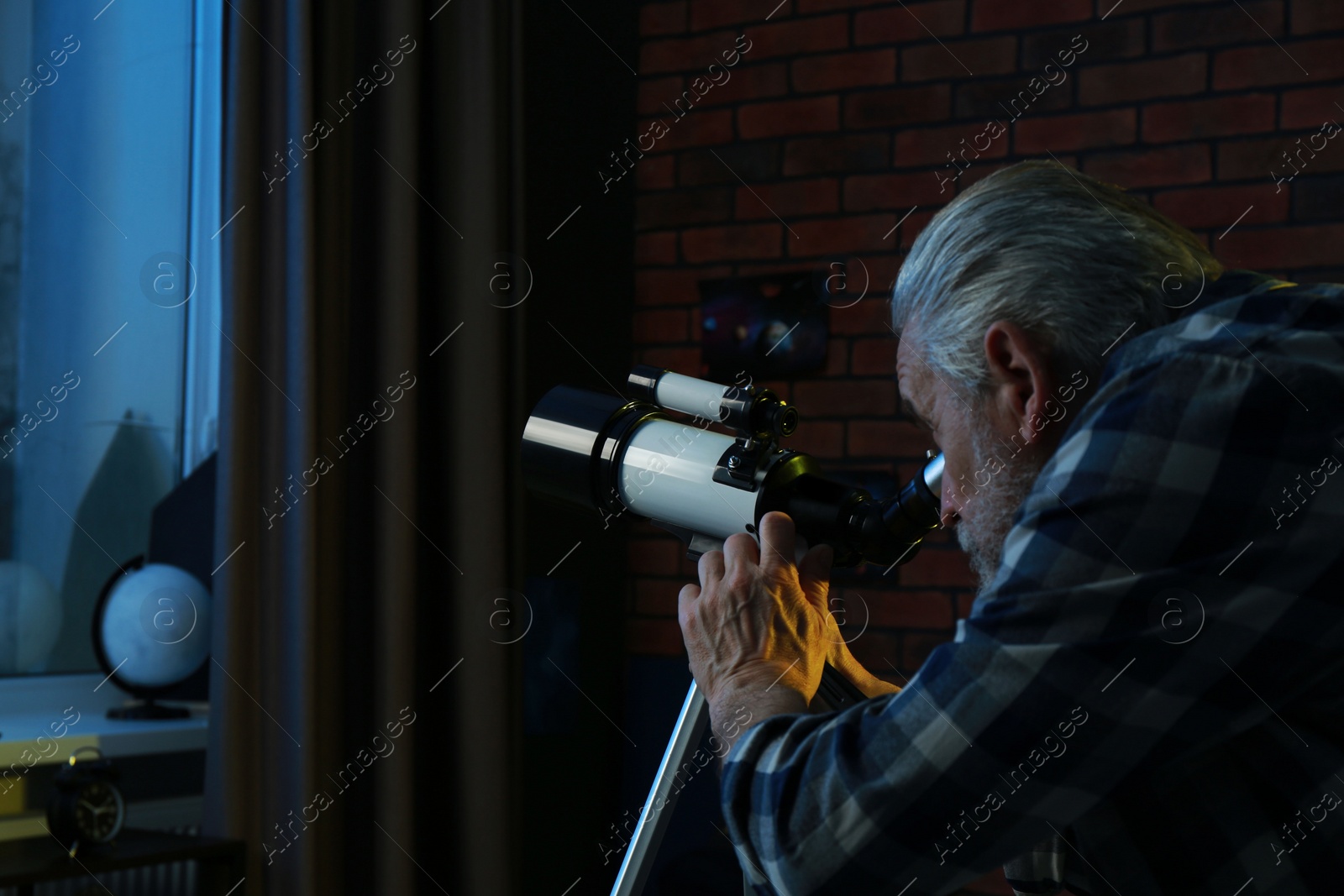 Photo of Senior man looking at stars through telescope in room