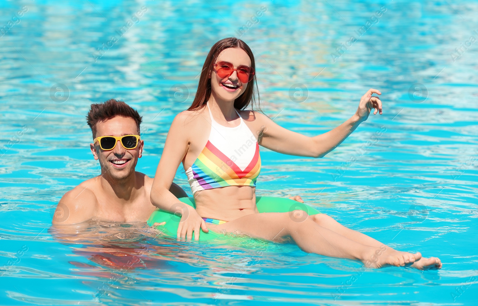 Photo of Happy young couple with inflatable ring in swimming pool