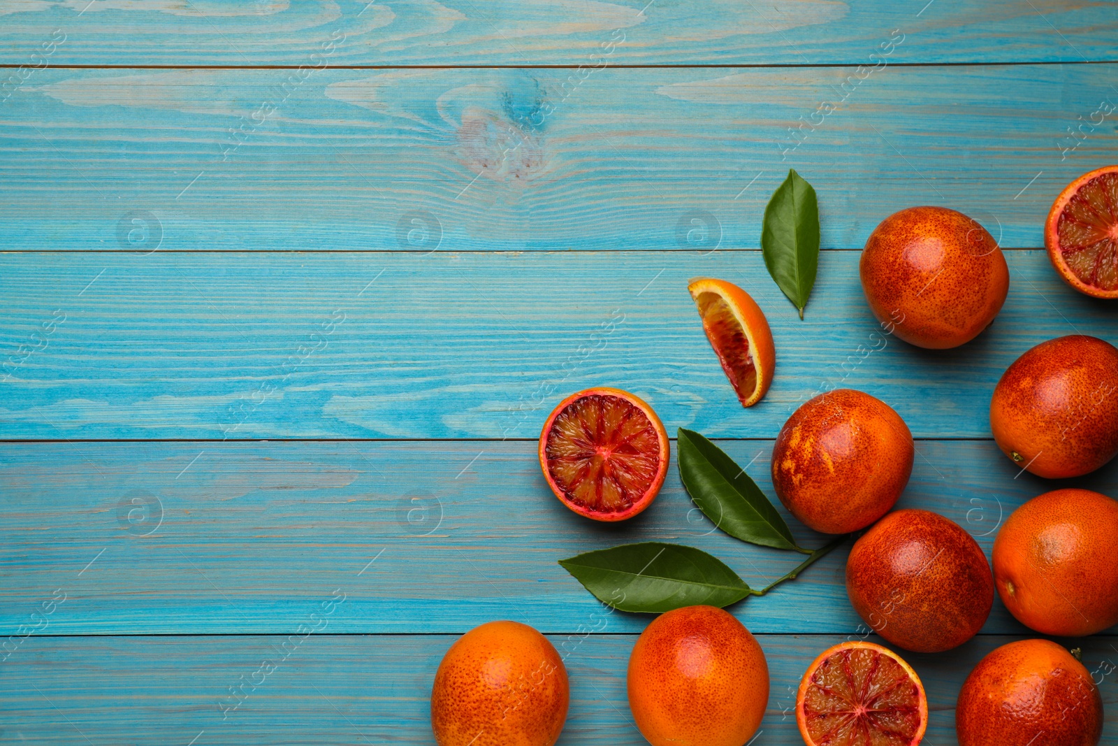 Photo of Many ripe sicilian oranges and leaves on light blue wooden table, flat lay. Space for text