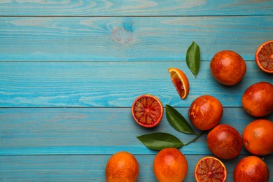Many ripe sicilian oranges and leaves on light blue wooden table, flat lay. Space for text