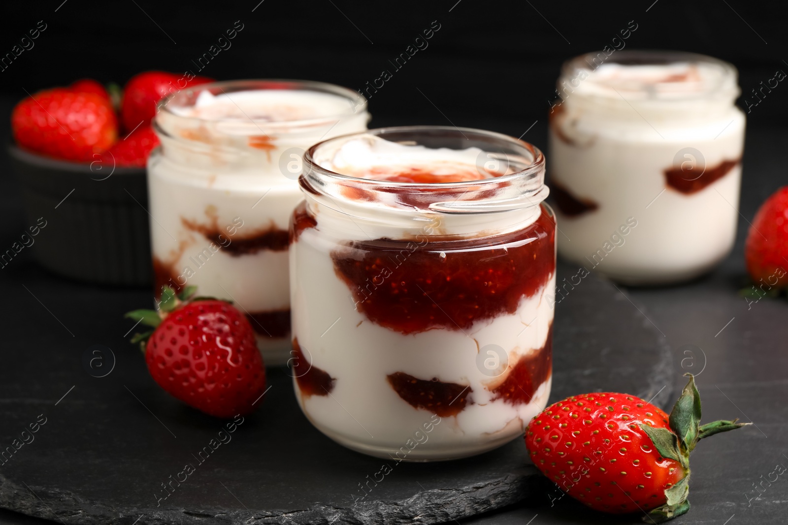 Photo of Tasty yoghurt with jam and strawberries on black table, closeup