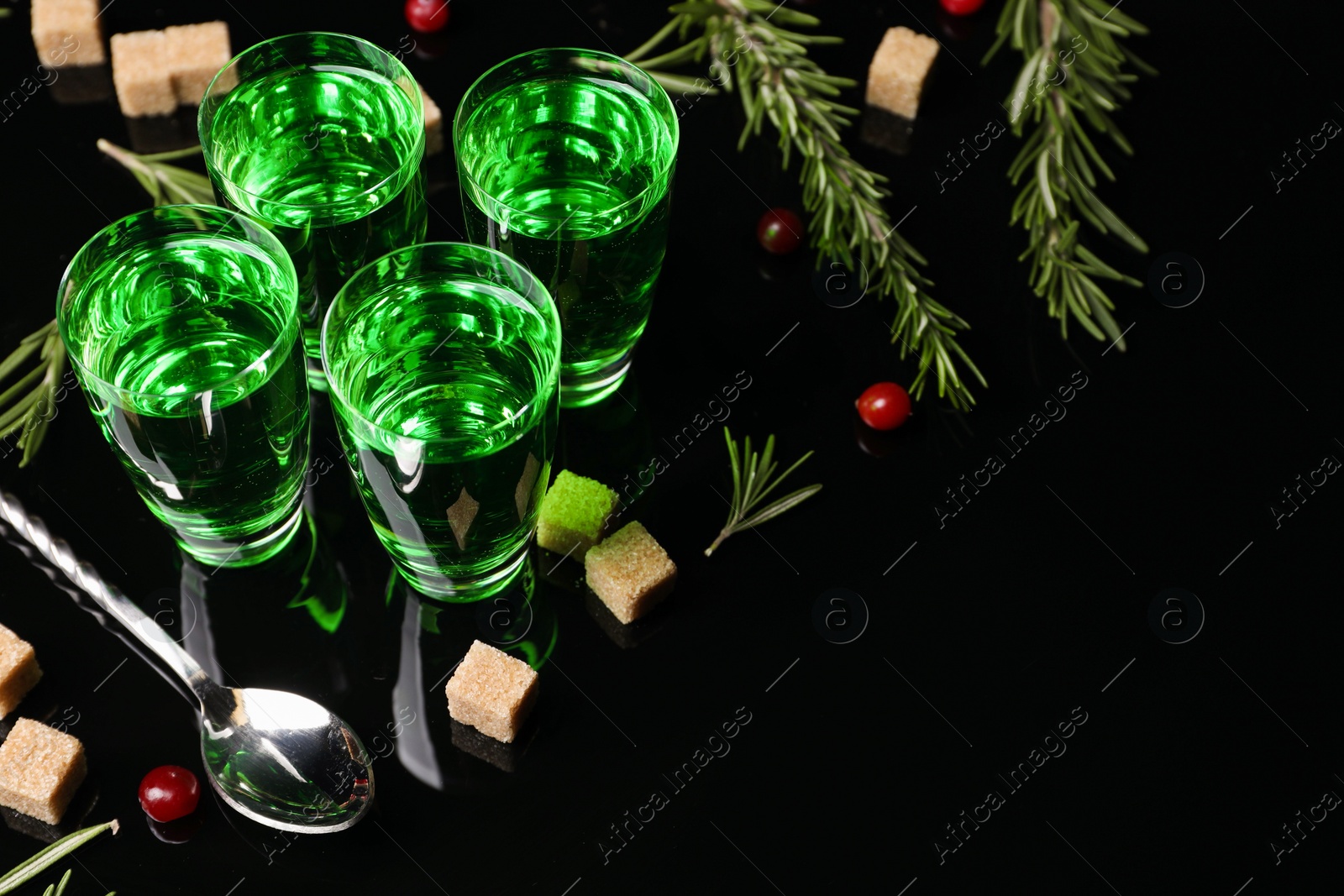 Photo of Absinthe in shot glasses, cranberries, rosemary and brown sugar on mirror table, space for text. Alcoholic drink