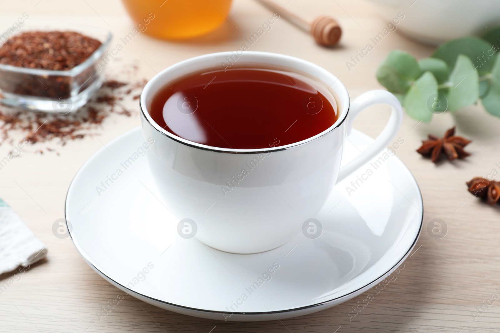 Photo of Freshly brewed rooibos tea, dry leaves and anise on white wooden table