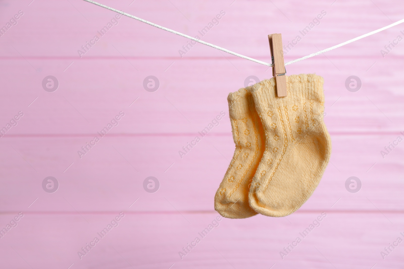 Photo of Pair of socks on laundry line against pink wooden background, space for text. Baby accessories