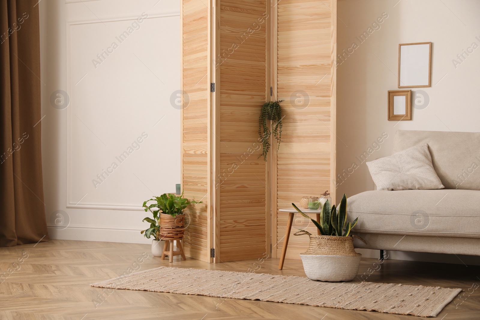 Photo of Stylish room with wooden folding screen and comfortable sofa near white wall. Interior design